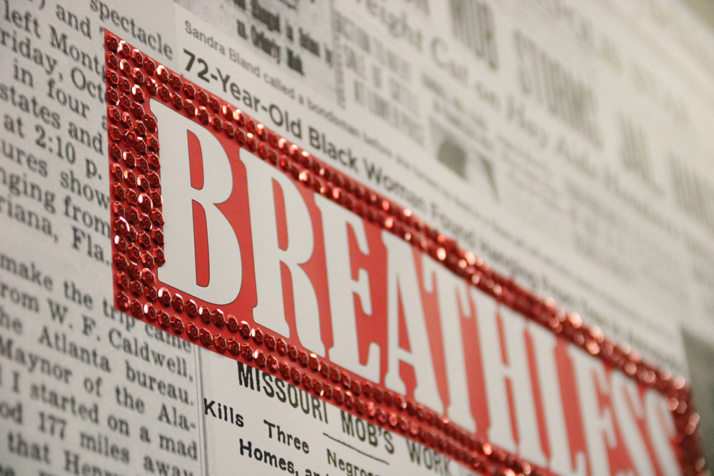 A close-up of a print resembling a newspaper. A red rectangle in the center of the image bordered by red rhinestones has white text that reads, "BREATHLESS."